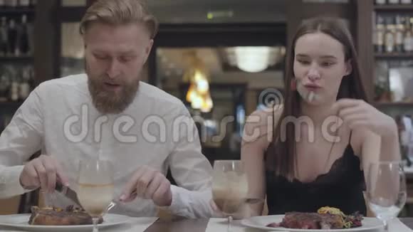 一位年轻可爱的黑发女人和留胡子的男人在餐馆或咖啡馆里吃晚饭或晚餐的肖像视频的预览图