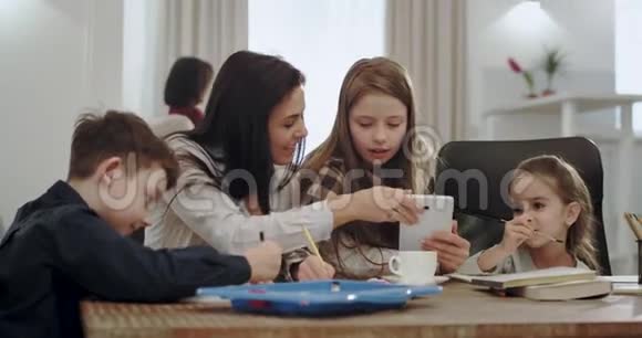 家庭作业时间成熟的母亲带着白色和大大的微笑帮助她的孩子做一些学校项目使用平板电脑视频的预览图