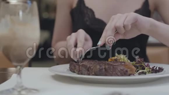 年轻女人的手在餐馆里切着美味的牛排盘子里放着蔬菜和树叶酒精饮料视频的预览图