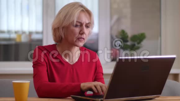 一位老白种人女商人在一间舒适的公寓里在笔记本电脑上打字在室内头痛的特写镜头视频的预览图