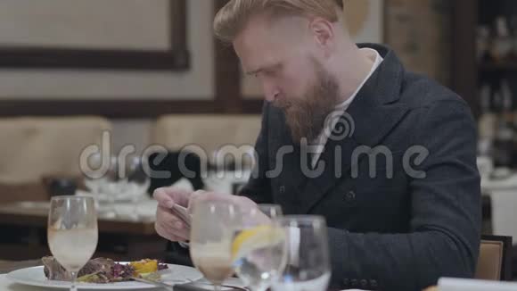 一位留着胡子的成功商人穿着时髦的夹克拿着手机坐在一个视频的预览图