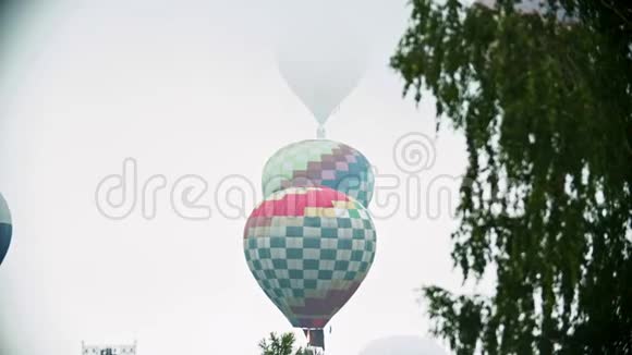 不同的彩色气球在白色的天空背景下飞过田野视频的预览图