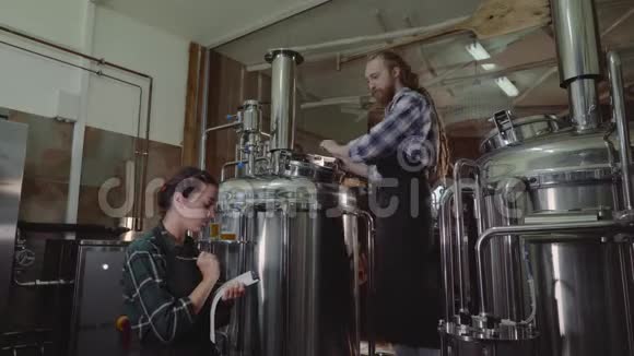 在啤酒厂或啤酒厂工作的有剪贴板的妇女啤酒厂工人打开一个啤酒桶的盖子在一个工艺啤酒视频的预览图