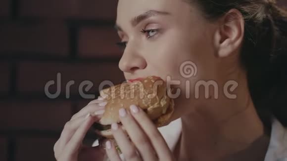 饥饿的女人在快餐店的砖墙背景下吃汉堡视频的预览图