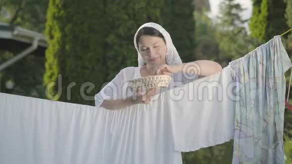 美丽的女人头上戴着白色披肩吃着樱桃看着相机微笑着在户外的晾衣绳上视频的预览图