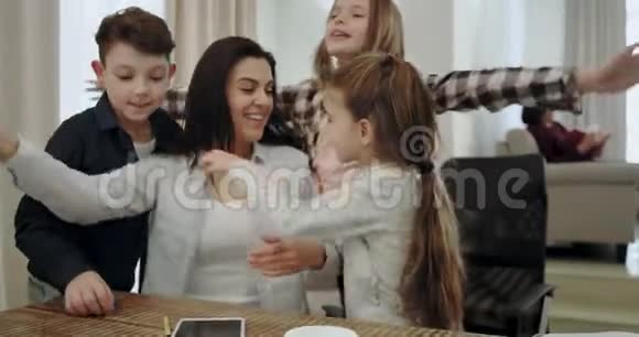快乐的母亲和她的三个孩子拥抱在一起就像一个友好的团队在客厅的桌子上而奶奶在读一本书视频的预览图
