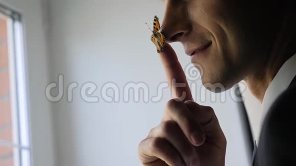一个年轻人把蝴蝶放在鼻子上蝴蝶坐在鼻子上不飞走他笑了拍得很好视频的预览图