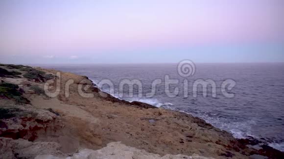 波在地中海上波浪撞击岩石海岸粉色日落视频的预览图