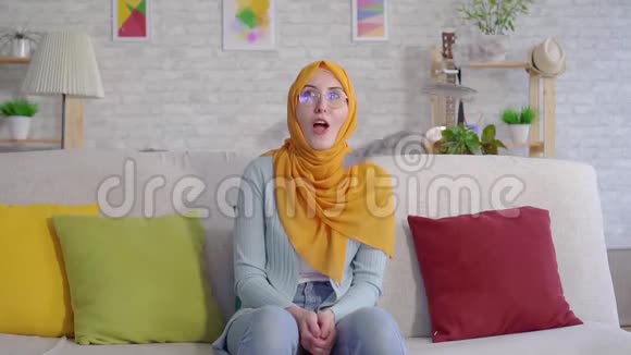 积极的年轻穆斯林妇女在家中坐在沙发上看到掉落的钞票视频的预览图
