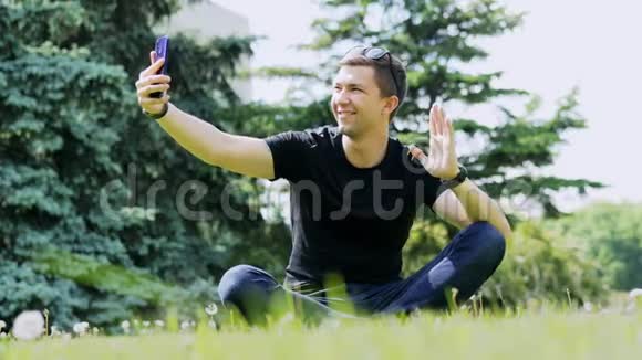 男人通过手机进行视频聊天坐在公园的草地上通过视频通话与朋友交谈视频的预览图