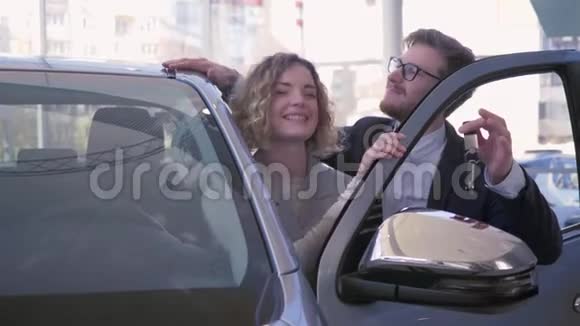 微笑的汽车买家的肖像年轻夫妇享受汽车并在销售中心的特写镜头钥匙车视频的预览图