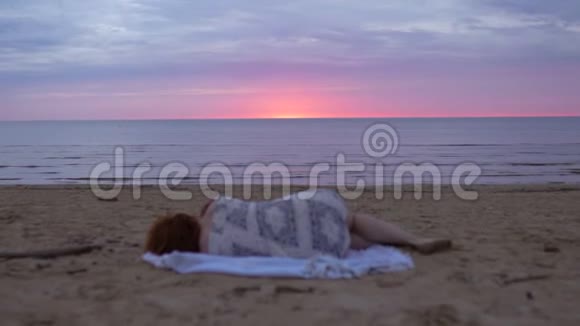 年轻女子穿着白色连衣裙躺在毯子上的前景中享受着罕见的发光的自然天空太棒了视频的预览图