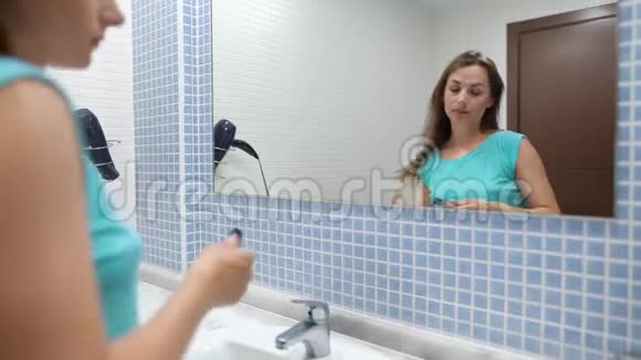 漂亮的女人在浴室镜子前用液体唇膏化妆嘴唇视频的预览图