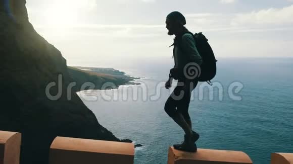 年轻自信的留着胡须的徒步旅行者的剪影背着背包走在加那利岛上高高的公路边缘视频的预览图