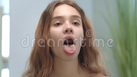 年轻女子张开嘴对着浴室的镜子望着舌头和喉咙视频的预览图