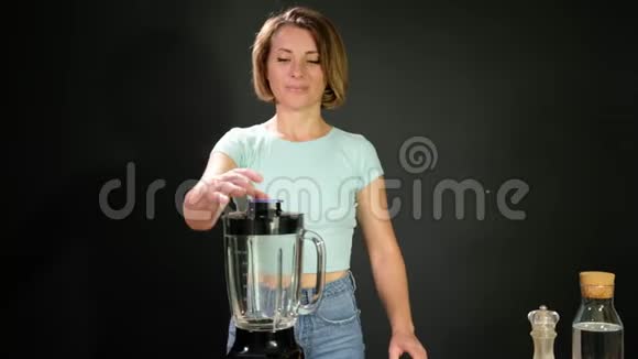 一个年轻的女人正在做未加工的西班牙凉粉她把西红柿放进搅拌机里视频的预览图