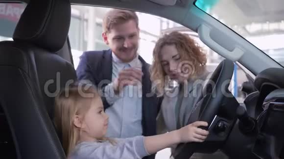 在经销商店买家用汽车时和爸爸妈妈一起在新车后面微笑着的小女孩视频的预览图