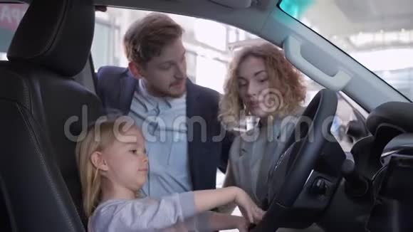 快乐的童年可爱的小女孩在汽车车轮后面和爸爸妈妈一起买家庭机器视频的预览图