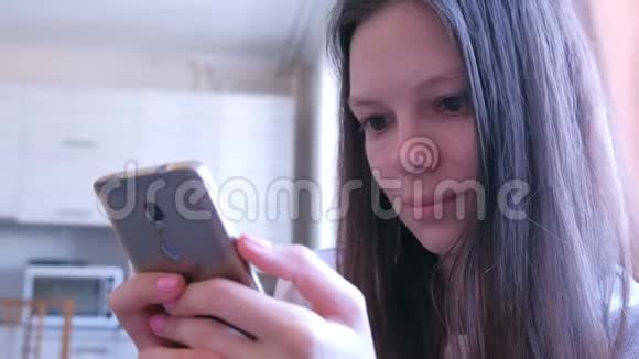 年轻女子正在家中厨房用智能手机浏览网页视频的预览图