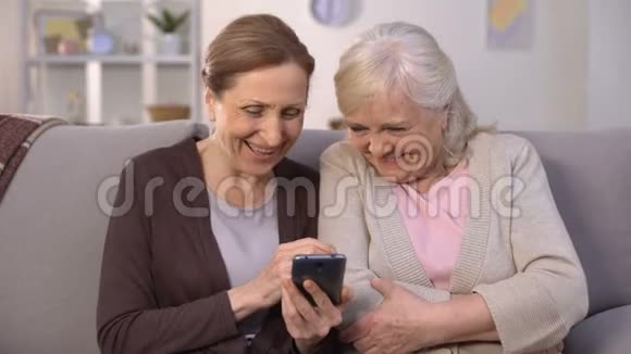 快乐的老女人看着智能手机上的照片笑着美好的回忆视频的预览图