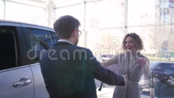 母亲节礼物迷人的男人把汽车送给快乐拥抱的女人并在汽车经销商处展示钥匙视频的预览图
