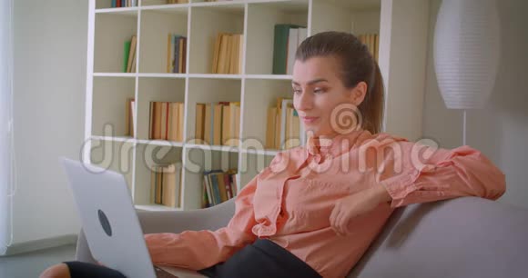 在笔记本电脑上工作的年轻漂亮女商人的特写镜头她看着相机兴高采烈地坐在电脑上视频的预览图