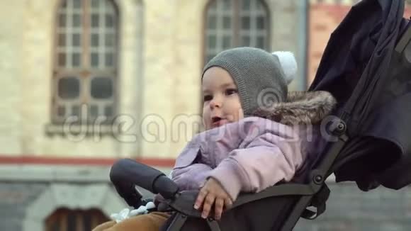 一岁女孩坐在婴儿车里的肖像把旅行的孩子关起来寒冷的天气4k视频的预览图