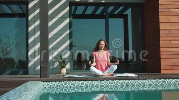放松的女人在游泳池附近冥想年轻女士做瑜伽练习视频的预览图