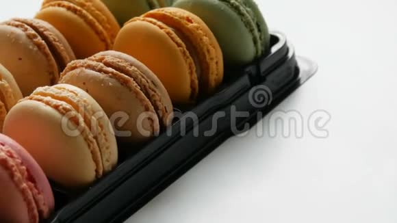 五颜六色的法国饼干通心粉在一个特殊的黑色盒子上的白色桌子礼品盒中的彩色蛋糕苹果视频的预览图