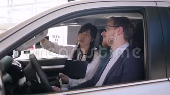 友好的女售货员亚洲裔建议客户坐在汽车沙龙在展厅卖车时握手视频的预览图