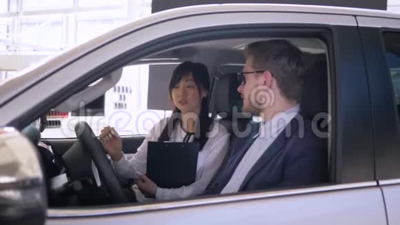 汽车生意成功的亚洲女售车商建议坐在汽车里面的男买家给钥匙和摇视频的预览图