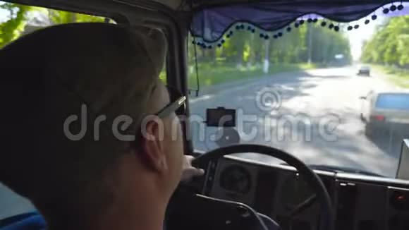 查看无法辨认的卡车司机在机舱内乘坐城市道路和享受旅程在阳光明媚的一天戴帽子的男人视频的预览图