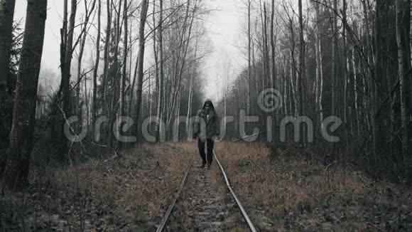 一个戴着防毒面具的人走在空寂的森林里废弃的旧铁路上视频的预览图