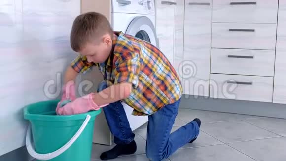 穿橡胶手套的男孩把布压在水桶上洗厨房的地板儿童的家庭责任视频的预览图