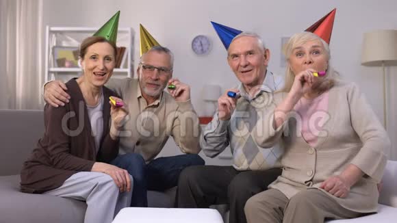 戴着生日帽的快乐老人在聚会上吹喇叭庆祝聚会视频的预览图