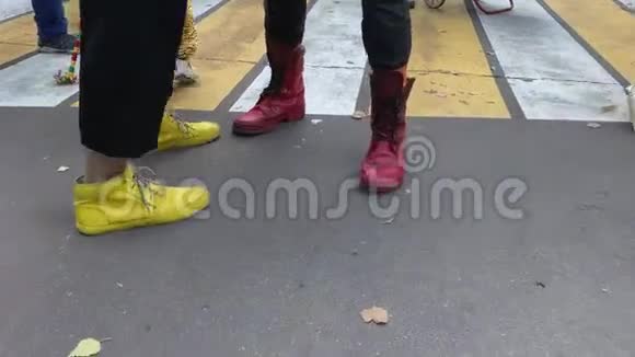 穿着五颜六色的黄色和红色靴子的小丑的腿和脚在沥青路上互相玩耍视频的预览图