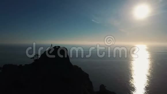 一个年轻女子在日落时靠海爬到山顶的剪影的史诗空中景色女士视频的预览图