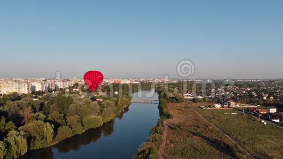 一个美丽的红色气球在傍晚飞过河流和城市视频的预览图