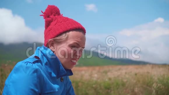 有趣的女孩站在阳光明媚的夏天金发女郎穿着蓝色外套戴着红色帽子嘴里放着一根棒棒糖视频的预览图