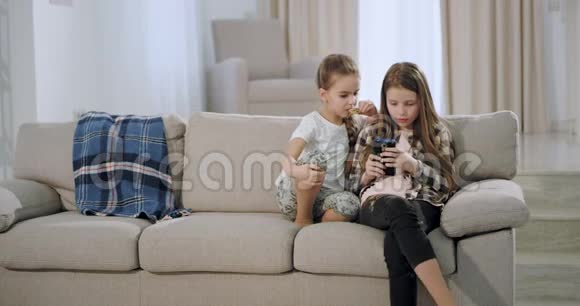 两个漂亮的姐妹坐在沙发上在一个宽敞的现代客厅里玩智能手机游戏非常视频的预览图