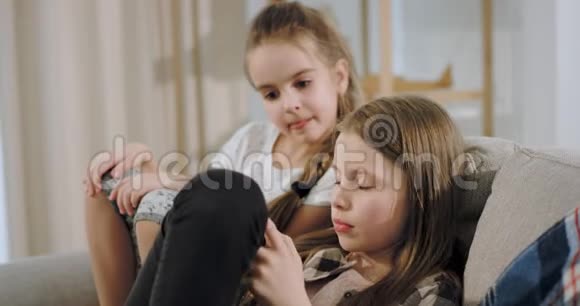 两个有魅力的女孩坐在沙发上玩智能手机游戏的肖像奶奶视频的预览图