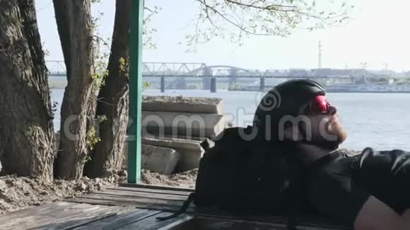 带胡须的自行车运动员在训练结束后躺在长凳上休息时喝着来自比顿的水城市和河流的背景视频的预览图