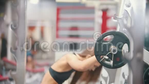 一位在健身房训练的女运动员在哑铃下把它放在肩上视频的预览图