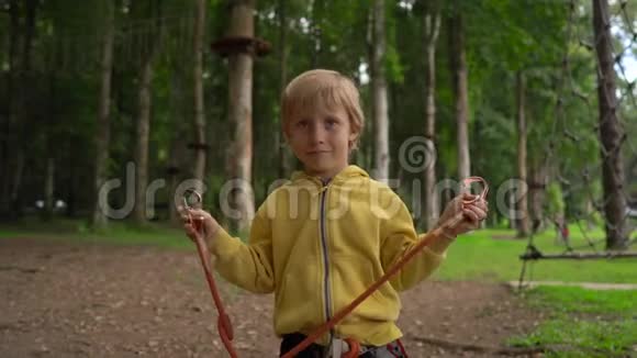 森林探险公园里的小男孩展示了他的安全装备户外游乐中心有攀岩活动视频的预览图