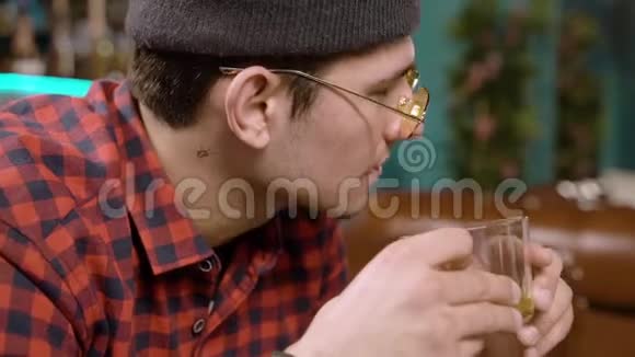 戴着帽子戴着太阳镜的年轻时髦男人在咖啡馆里喝绿茶视频的预览图