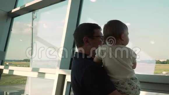 父子俩透过玻璃窗看着飞机在机场和婴儿一起旅行视频的预览图