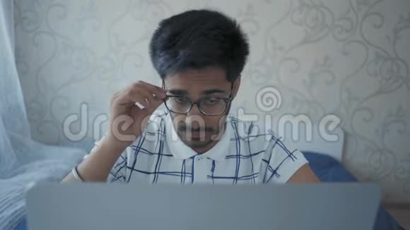 特写镜头印度学生坐在笔记本电脑前摘下眼镜用手揉脸视频的预览图