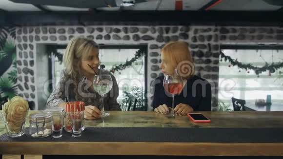 两个女朋友坐在酒吧柜台旁喝着鸡尾酒进行有趣的谈话视频的预览图
