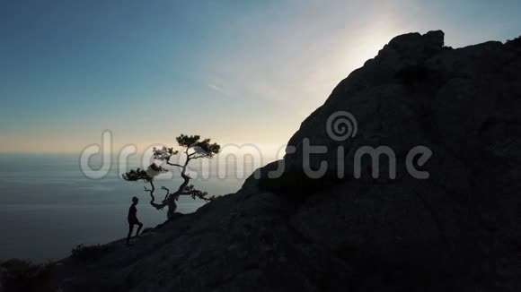 一位年轻女子在日落时靠海爬到山顶的剪影女士视频的预览图
