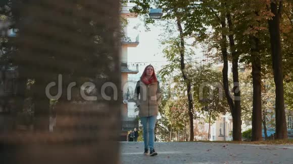 穿着夹克的年轻漂亮的红头发女人正沿街走着视频的预览图